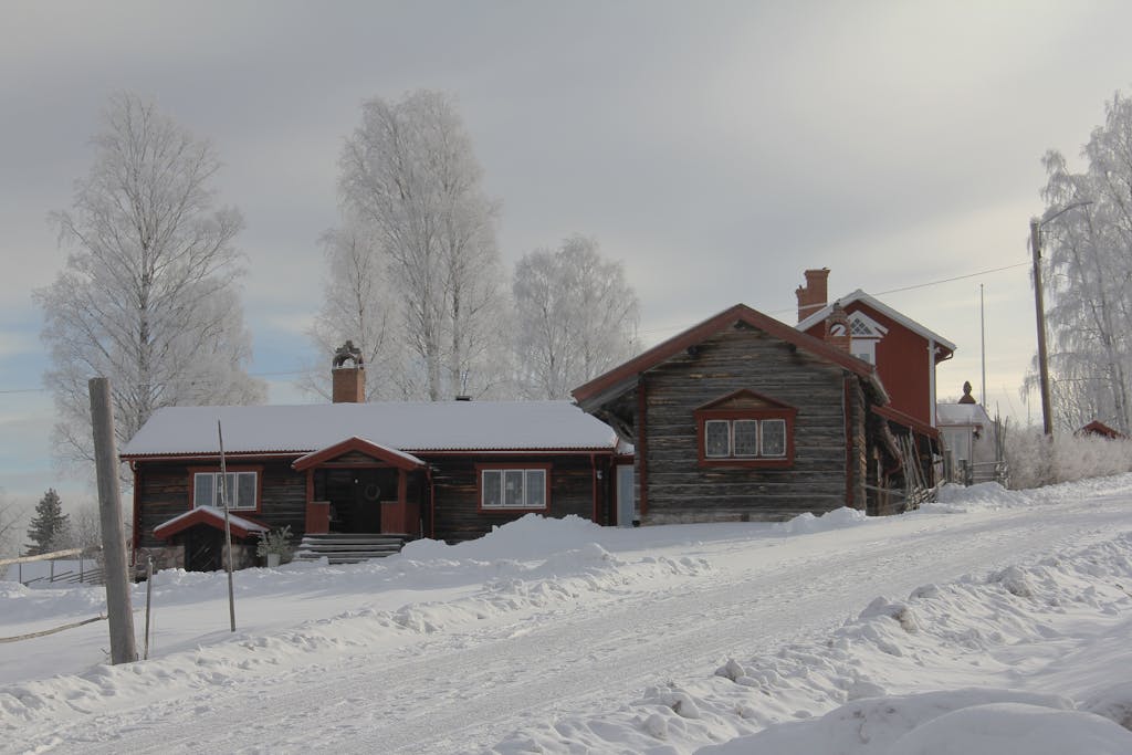 A picturesque winter scene of a traditional wooden cottage in a snowy Swedish landscape.
