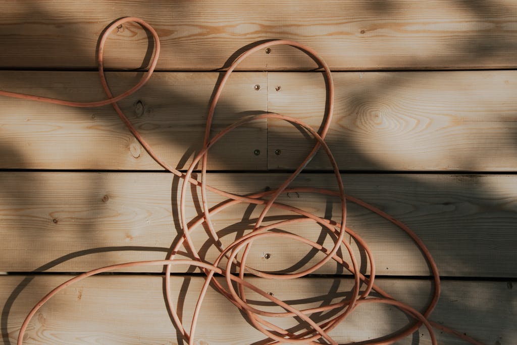 An orange cable is tangled on a sunlit wooden plank surface with shadows, creating a rustic and artistic look.