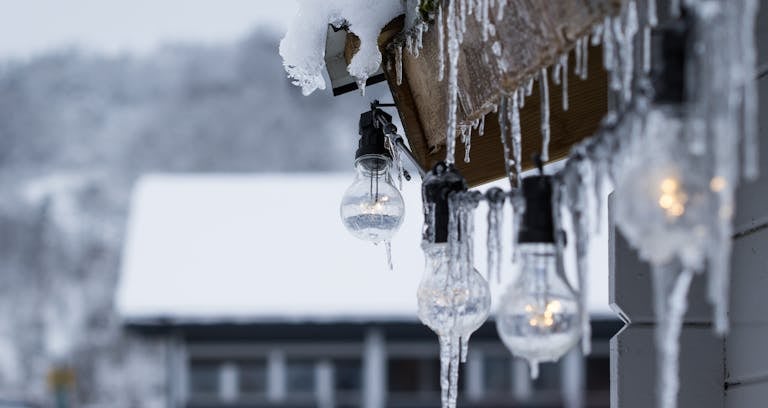 Close-up of hanging lightbulbs covered in icicles against a snowy winter backdrop.
