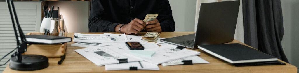 Serious businessman counting money at a desk in a modern office setting.